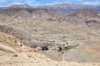 Auf historischen Pfaden  Fast alle Touristen, die in Arica landen, nehmen die nördlichste Stadt Chiles als Ausgangspunkt, um den beeindruckenden Parque Nacional Lauca zu besuchen. Die meisten belassen es bei dem Abstecher in den 140 km entfernten Park und kehren anschließend wieder an die Küste zurück, um der Pan Americana Richtung Süden zu folgen. Einige wenige bleiben aber im Altiplano und legen die Strecke nach Iquique in meist atemberaubenden Höhen von ~4500 m zurück.  Um aber den Lauca NP zu erreichen, gilt es erst einmal, den Anstieg von Meereshöhe auf über 4000 m zu bewältigen. Dabei folgt man einer hervorragend ausgebauten Asphaltstraße, die kaum vermuten läßt, dass man sich auf uralten Wegen indianischer Handelskarawanen bewegt. Bereits im 12. Jahrhundert gab es einen regen Austausch von Waren der küstenbewohnenden Fischer und den im Hochland lebenden bäuerlichen Kulturen der Aymara Indianer, die dort Kartoffeln und Mais anbauten sowie Lamas züchteten. Da die späteren spanischen Konquistadoren kein Gold vorfanden, blieben die hier lebenden Völker weitgehend unbehelligt – abgesehen von dem unvermeidlichen Überstülpen des katholischen Glaubens, wovon heute noch die kleinen weißgekalkten Kirchen in den Bergdörfern Zeugnis ablegen.  An einigen Stellen gibt es aber noch Hinweise auf die prähistorischen Kulturen, deren Verbreitungsgebiet sich über die heutigen Grenzen hinaus weit nach Peru und Bolivien erstreckte. Bereits kurz hinter Arica sieht man mächtige Felszeichnungen an den kahlen Hängen rechts der Straße und nach ca. 75 Kilometern erreicht man eine alte indianische Befestigungsanlage, die 'Pukará de Copaquilla'. Auch wenn das Foto die Überreste der Anlage nicht zeigt, kann man doch wunderbar von der Straße aus den tiefen Taleinschnitt betrachten, an dessen Grund noch heute der grüne Bewuchs der lebenspendenden Oase leuchtet. Exemplarisch sieht man hier auch die typischen Strukturen der ins Hochland ansteigenden Kordilliere mit ihren vielfältigen Fels- und Sandtönungen, die die Einöde abwechslungsreich auflockern.