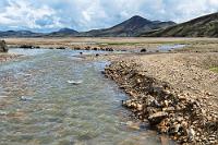 Ausgeschlossen  Es führt eine hölzerne Fußgängerbrücke über einen Arm des verzweigten Flußlaufes, über die wir auf die Seite des Campingplatzes gelangen. Leider passiert schon seit einiger Zeit kein hochbeiniger Jeep die Fahrspur, die von links kommend in den dunklen Spuren ihre Fortsetzung findet, sonst sähe man, wie tief es in der Flussmitte wirklich wird. Nix für unseren Duster!  Aber auch nix für unsere Füße, denn der einzige Fussweg zum Campingplatz steht inmitten einer sumpfigen Grasfläche ca. 10 cm tief unter Wasser. Der, laut Reiseführer, "beliebte kurze Ausflug auf den 946 m hohen Berg Bláhnúkur mit der fantastischen Aussicht auf den Schwefelberg" und ein dampfendes Hochtemperaturgebiet muß daher leider entfallen, denn es werden am Campingplatz keine Ersatzschuhe gestellt.