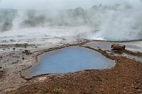Blesi  Ein bißchen weiter auf dem Rundweg gelangt man zur Quelle Blesi, von der aber heute nicht viel zu sehen ist, denn das brodelnde heiße Wasser produziert so viel Dampf, dass kein vernünftiges Foto gelingt. Man kann sich aber mit dem ruhigen Abflusstümpel trösten, dessen hübsches Türkis vorteilhaft mit den braunroten Lavakieseln am Rande kontrastiert.  Wir sind nicht zu früh hier, denn inzwischen hat sich der Besucherkreis um den Strokkur fast nahtlos geschlossen – was wegen der Windstille möglich ist –, und zuverlässig läßt einen das aufbrausende "Aaaah" und "Oooh" den aktuellen Ausbruch akustisch nachvollziehen :-).