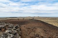 Braunstein  Die nächste Station ist der Saxhóll Vulkan, der über eine kurze Zufahrt vom Útnesvegur zu erreichen ist und eine relativ flache Steigung hat, über die eine gewundene Treppe nach oben führt. Mir steckt noch die Halbkilometersteigung an der Rauðfeldsgjá in den Knochen, so dass ich Maren bei der Ersteigung des Vulkans souverän den Vortritt lasse. Ich versuche mich derweil an Luftaufnahmen, die aber aufgrund des heftigen Windes nicht so richtig gelingen wollen.