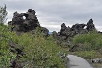 Dimmuborgir  Diesmal waren es nicht Krafla Vulkane, sondern die östlich des Mývatn gelegenen Kraterreihen Þrengslaborgir und Lúdentsborgir, deren Lava hier vor 2300 Jahren über sumpfigen Boden floß. Es kam zu keinen Explosionen, aber der Dampf des unter der Lava begrabenen, kochenden Wassers bahnte sich seinen Weg über mehrere Meter durchmessende Schlote nach oben. Die noch heiße Lava unter der erstarrenden Kruste floß ab und hinterließ einen Hohlraum, in den die Lavadecke später einbrach und nur die bizarren Reste der Schlote stehen ließ. Leider hat das Wetter die Vorhersage nicht gelesen, denn auch nach 10:00 Uhr bleibt es durchgehend bewölkt. Außer uns und den Passagieren diverser Reisebusse sind jetzt auch wieder Milliarden der Mückenviecher unterwegs, so dass wir trotz Moskitohüten den Rundweg stark abkürzen.