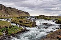 Fossálar Fall  Nur einen Kilometer weiter bremsen wir kurz entschlossen auf der 1, nachdem wir vor den Berghängen einen breiten Wassersturz bemerken, zu dem auch der direkt an der Straße gelegener Parkplatz gehört, den wir eben passiert haben. Schnell gewendet auf der verkehrsarmen Ringstraße, gesellen wir uns zu dem bisher einzigen Fahrzeug, das hier bisher steht (unnnötig zu erwähnen, dass der uns sattsam bekannte Magneteffekt spätestens mit unserer Ankunft einen Volksauflauf zur Folge hat – wie jetzt auch wieder :-). Höchst sehenswert stürzt hier ein Abfluss des Eyjalon Schmelzwassersees über mehrere Stufen Richtung Meer.