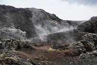Fußbodenheizung  Unter dem Krafla Massiv befindet sich in 3 km Tiefe eine Magmakammer, die mit ihren Ausbrüchen und Ausflüssen seit geschichtlichen Zeiten die Vulkanlandschaft bis heute geformt hat. Die letzten, von Erdbeben bis zu einer Stärke 4 begleiteten Ausbrüche, die sogenannten 'Krafla-Feuer', ereigneten sich von 1975 bis 1984 und sind verantwortlich für die immer noch warmen, tiefschwarzen Lavafelder rund um den Leirhnjúkur. Der weiterführende Weg ist mitunter steil und erfordert das Klettern über zum Teil sehr scharfkantige Lava, so dass wir uns entscheiden, zum Parkplatz zurückzukehren.  Es geht auf dem gleichen Weg entlang des langgestreckten Leirhnjúkur zurück und jetzt sehen wir auch, wo die Leute aus den Fahrzeugen am Parkplatz abgeblieben sind. Sie haben den Lavaweg weiter verfolgt und stehen jetzt winkend auf dem Gipfel des orangegelben Berges.
