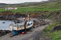 Gestrandet  Es ist Zeit für den Rückweg. Vorbei an dem mit morbidem Charme vor sich hinrostenden Fischkutter gelangen wir zu unserem Auto, in dem wir gleich nach dem Anlassen als Erstes die Heizung auf Maximum stellen. Natürlich dauert es ein bißchen, bis es warm wird, aber man kann gar nicht früh genug damit anfangen...  Die Straße hatte auf der Herfahrt nicht weit entfernt ein Flüsschen gekreuzt, dessen kiesiges Flußbett einem Gebirgstal entsprang, welches sich in Farbe und Beschaffenheit deutlich von den umliegenden Hängen abhob. Der Lundifelsen hatte da noch Priorität, wir haben uns aber fest vorgenommen, auf dem Rückweg dort noch einmal halt zu machen.