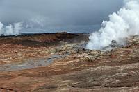 Gunnuhver  Unerwartet sehen wir wenige Kilometer weiter dicke weiße Dampfwolken über die Straße wabern. Ein Hinweisschild weist auf Gunnuhver, das größte Schlammquellgebiet Islands hin und wir biegen sofort auf die schmale, von löchrigem Asphalt bedeckte Straße ab, die an einem Parkplatz endet, von dem aus einige Holzbohlenwege in das dampfende, stark nach Schwefelwasserstoff riechende Gelände führen. Überall brodelt und blubbert es, bei genauerem Hinsehen wird der Eindruck unverfälschter Natur aber durch die nahebei befindlichen Gebäude des örtlichen Geokraftwerks Suðurnes etwas getrübt, aus dessen Schornsteinen ebenfalls der weiße Dampf quillt. Immerhin verschafft uns das durch häufige Erdbewegungen ständigem Wandel unterworfene Gebiet einen ersten Eindruck des isländischen Vulkanismus.