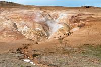 Heiße Spalte  Vorbei an dem 60 MW Geothermalkraftwerk "Kröflustöð", dessen zu den Zapfstellen führende Dampfrohre in einem umgekehrten U über die Straße führen, erreichen wir den Parkplatz Leirhnjúkur. Gelegen auf einer schwarzen Lavaergußebene in über 600 m Höhe, ist die Schneesaison noch nicht ganz vorbei, so dass wir auf dem Pfad zum lehmgelben Leirhnjúkur durch einige Senken stapfen müssen, deren angetauter Schnee uns schnell nasse Schuhe beschert.  Es hat sich etwas zugezogen und nur gelegentlich blitzt die Sonne auf –  die  Gelegenheit, die dem Bergriss entweichenden Dämpfe ordentlich auszuleuchten.
