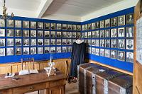 Honoratiorenkabinett  Die Front des Gehöftes bilden sechs Einzelhäuser, von denen die ersten drei Lagerräume und eine Schmiede beherbergen, gefolgt von dem Haupthaus mit dem Eingang zu den dahinter, links und rechts vom Gang aufgereihten Wohnhäuschen. Der vierte, separate Eingang, gehört zu einem Gästezimmer, welches auch vom Zentralgang zugänglich ist, während das Fünfte, auf dem ersten Foto nur noch angeschnittene Häuschen, als Brennstofflager diente.  Das linksseitig vom Zentralgang befindliche Gästezimmer zeigt, wie alle weiteren Räumlichkeiten, den Einrichtungszustand aus der Mitte des 19. Jahrhunderts und ist aktuell an den Wänden mit Bildern wichtiger Persönlichkeiten "Skagafjörðurs" aus dem 19. und 20. Jahrhundert bestückt, die in diesem prominenten Gehöft als Gäste weilten. Auch scheint der Talar darauf hinzuweisen, dass der Pfarrer der angegliederten Kirche zumindest zeitweilig hier gewohnt hat.