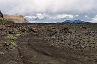 Knüppelpiste 208  Unsere Planung mit den drei Resttagen fürs Hochland hat bis jetzt ganz gut funktioniert. Abgesehen von Tag 1, den wir wegen Starkregen nach der "Allmännerschlucht" abbrechen mußten, haben wir zumindest gestern das Versäumte und mehr wieder aufgeholt. Der vorletzte Tag soll noch einmal auf einer anderen Strecke ins Hochland führen, wofür uns die Wetterapp brauchbares Wetter verspricht. Die ersten Eindrücke sind nicht motivierend, um Reykjavik herum liegen die Wolken fast auf und es tröpfelt, aber wir haben ja auch noch knapp 200 km vor uns. Die wir prompt um ein paar weitere Kilometer verlängern, da uns "Organic Maps" auf die F225 führt, auf der wir schnellstens wieder umkehren, bevor wir vor einer unpassierbaren Furt stehen. Auch die asphaltierte 32, die wir stattdessen nehmen, mündet später auf der 208, einer Schotterpiste, die eigentlich nur noch aus groben Steinen, Schlaglöchern und Lavabrocken besteht.