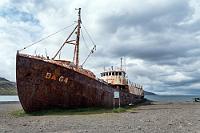 Kultobjekt  Nur wenig später am Ende des Fjords angekommen, kommt schon wieder die Sonne durch, so dass es sich lohnt, den malerisch vor sich hinrostenden Heringsfischer ebenfalls mal abzulichten. 'Ebenfalls' deshalb, weil auch jetzt ein paar Autos auf dem Parkplatz halten, deren Insassen sich zu abwechselnden Selfies vor dem Kahn versammeln. Wobei wir zugeben müssen, das es sich bei "Garðar BA 64" wirklich um ein unwiderstehliches Motiv handelt. 1912 in Norwegen gebaut und als Walfänger im Einsatz, kam das Schiff 1945 nach Island, wo es walfreundlicher als Heringsfischer eingesetzt wurde. 1981 nutzte man dann ein Fjordhochwasser, um das ausgediente Schiff über einen extra gegrabenen Kanal auf das Festland zu setzen, wo es seitdem als morbides Denkmal seinen Ruheplatz gefunden hat.