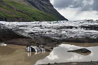 Langer Auslauf  Umgeben von mehreren kahlen Hügeln, die man mit wenig Anstrengung erklimmen kann, hat man einen fantastischen Ausblick auf den ockerfarbenen See und den langgestreckten, vielfach gebrochenen und aufgefalteten Ausläufer der Gletscherzunge, die sich noch weit in das vorgelagerte Flachland hinein entlang der gegenüberliegenden Bergflanke erstreckt. Noch immer weht nur wenig Wind und ich ärgere mich, tatsächlich mein fliegendes Auge im Auto vergessen zu haben. Nun, Fotomotive gibt es auch so genug und mit der Absicht, nach dem Einchecken im Hotel nochmals – diesmal mit der Drohne – hierher zurückzukehren, wandern wir erstmal zum Parkplatz zurück.