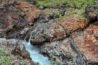 Panta rhei  Auch hinter der Brücke strömt die Hvitá, teilweise in Nebenflüsschen aufgetrennt, durch ein enges Felskorsett, bevor sich der Fluß zu der Breite weitet, in der er die Fälle passiert. Lediglich auf den hölzernen Stegen erreichbar, die nicht verlassen werden dürfen, bietet sich den Besuchern an vielen Stellen ein farbiger Einblick in die vulkanische Natur der Felslandschaft mit eingbetteten Schichten prähistorischer Ablagerungen.