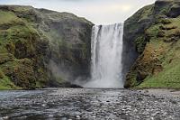 Remove Tool  So nennt sich ein höchst nützliches KI-Werkzeug in Photoshop, welches ungemein hilfreich ist, wenn es z.B. gilt, wichtige Motive hinter einer Mauer von Menschen sichtbar zu machen :-) Wir fahren weiter auf der Küstenstraße, rechtsseitig begleitet von wechselnden Aussichten auf das Meer, während sich auf der linken Seite die karstigen Klippen des Eyjafjallajökull Massivs erheben. Immer noch grübeln wir vor uns hin, wie eine Reise ohne Videokamera überhaupt noch sinnvoll sein kann, als mir plötzlich die Erleuchtung kommt: Obwohl nie genutzt, verfügen doch meine beiden Nikons ebenfalls über einen Videomodus! Da heute Wasserfall-Tag ist, schwenken wir nach nur 30 Kilometern wieder nach links von der Straße und haben unmittelbar den mächtigen Skógafoss vor uns. Hier ist es noch voller als am Seljalandsfoss. Eine erkleckliche Anzahl unserer Mittouristen hat sich über die gesamte, flache Flußbreite vor dem Fall verteilt. Ich weiche lieber weit zurück, denn damit werden die Rücken ganz klein und die KI hat ein leichtes Spiel mit ihnen – wie man sieht, erfolgreich ;-).