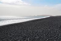 Reynisfjara Black Beach  Zum Abschied vom schwarzen Strand noch ein Panorama Richtung Westen bis hin zu den vom Dunst umhüllten Felsen der Klippen von Dyrhólaey. Sehr schön demonstriert diese Aufnahme den wahren Charakter des Küstenstreifens, der von der Kieselhaftigkeit mit zunehmender Entfernung zum 'Sandstrand' mutiert. Wie lange mag es gedauert haben, bis das andauernde Erosionswerk von Wetter und Wasser aus dem harten Vulkangestein diese Küsten gemahlen hat?  Inzwischen ist es 17:00 Uhr geworden und obwohl es wegen der jahreszeitlich langen Tage noch etliche Stunden hell bleibt, haben wir für heute unser Sightseeing Soll erfüllt. Außerdem liegen noch 80 km vor uns, bis wir unsere heutige Unterkunft erreichen.