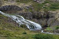 Small Dynjandi  Zuvor hat Maren noch den QR-Code mit ihrem Tablet fotografiert und hofft, die Rechnung am Abend im Hotel über die WLAN-Verbindung begleichen zu können. Da das Nummernschild parkender Fahrzeuge auf den meisten gebührenpflichtigen Plätzen mit einer Kamera erfasst wird, sollte man die Gebühr nicht schuldig bleiben.  Wir müssen einen halben Kilometer wieder zurück auf den Vestfjarðarvegur, der sich entlang des Flüsschens Sviná, vorbei an einem aus mehreren flachen Stufen bestehenden Wasserfällchen namens "Small Dynjandi" in die Höhe windet, bevor er nach Süden abbiegt und für die nächsten 40 km durch bergiges Binnenland führt, bis er die Küste wieder erreicht.