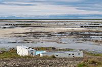 Wieder auf Kurs  Wir wenden, fahren ein Stück zurück, biegen wieder auf die 62 ein und nachdem wir die Hügelkette des südlichsten Ausläufers der Westfjorde überwunden haben, liegt der Breiðafjörður vor uns. Die Straße folgt der Küste und nach kurzer Zeit erreichen wir das Örtchen Vesturbyggð am Rande einer großen Meeresbucht. Es ist gerade Ebbe und die Bucht ist fast trocken gefallen. Wir halten auf dem kleinen Parkplatz gegenüber des Ortes, der sich entlang der linken Straßenseite hinzieht, oberhalb von ein paar Containern. Erst als wir aussteigen, werden wir des Schwimmbeckens gewahr, welches hinter den Containern am Buchtstrand platziert ist.